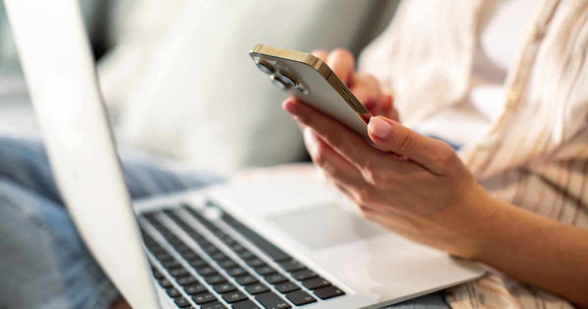 Close-up of hands using mobile phone and open laptop