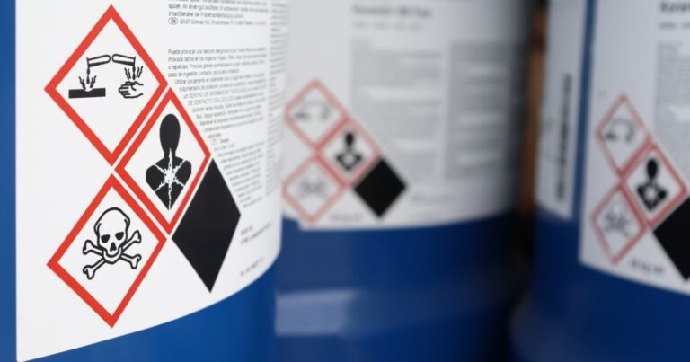 Hazardous chemical labels on containers contain images. Fine print is in soft focus and not readable.